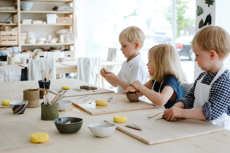 Lapset tekevät savitöitä puisten pöydän ääressä