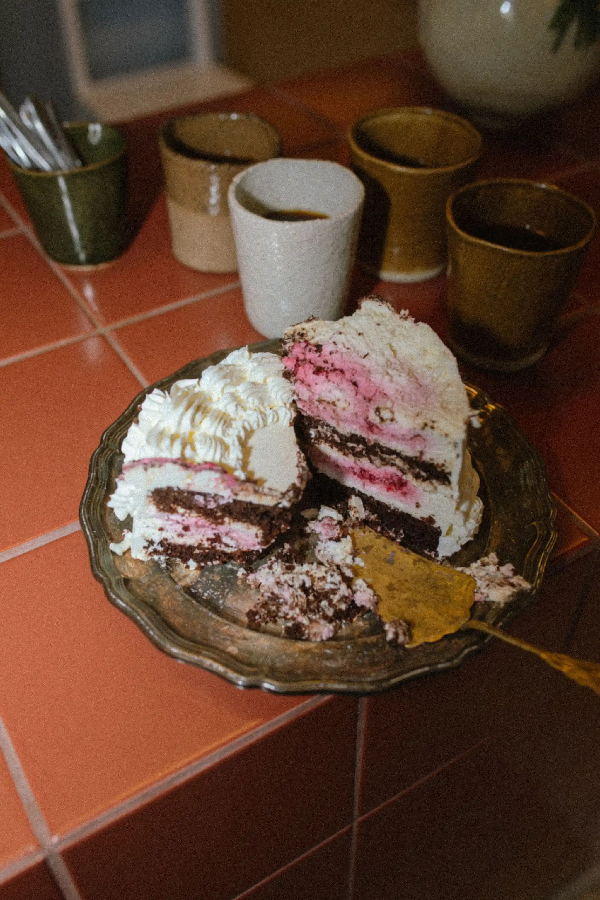 Herkullinen kakkutarjoilu ja käsintehtyjä keraamisia mukeja studion työtasolla.